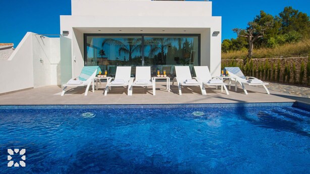 Un área de piscina moderna con sillones blancos y una piscina azul cristalina.