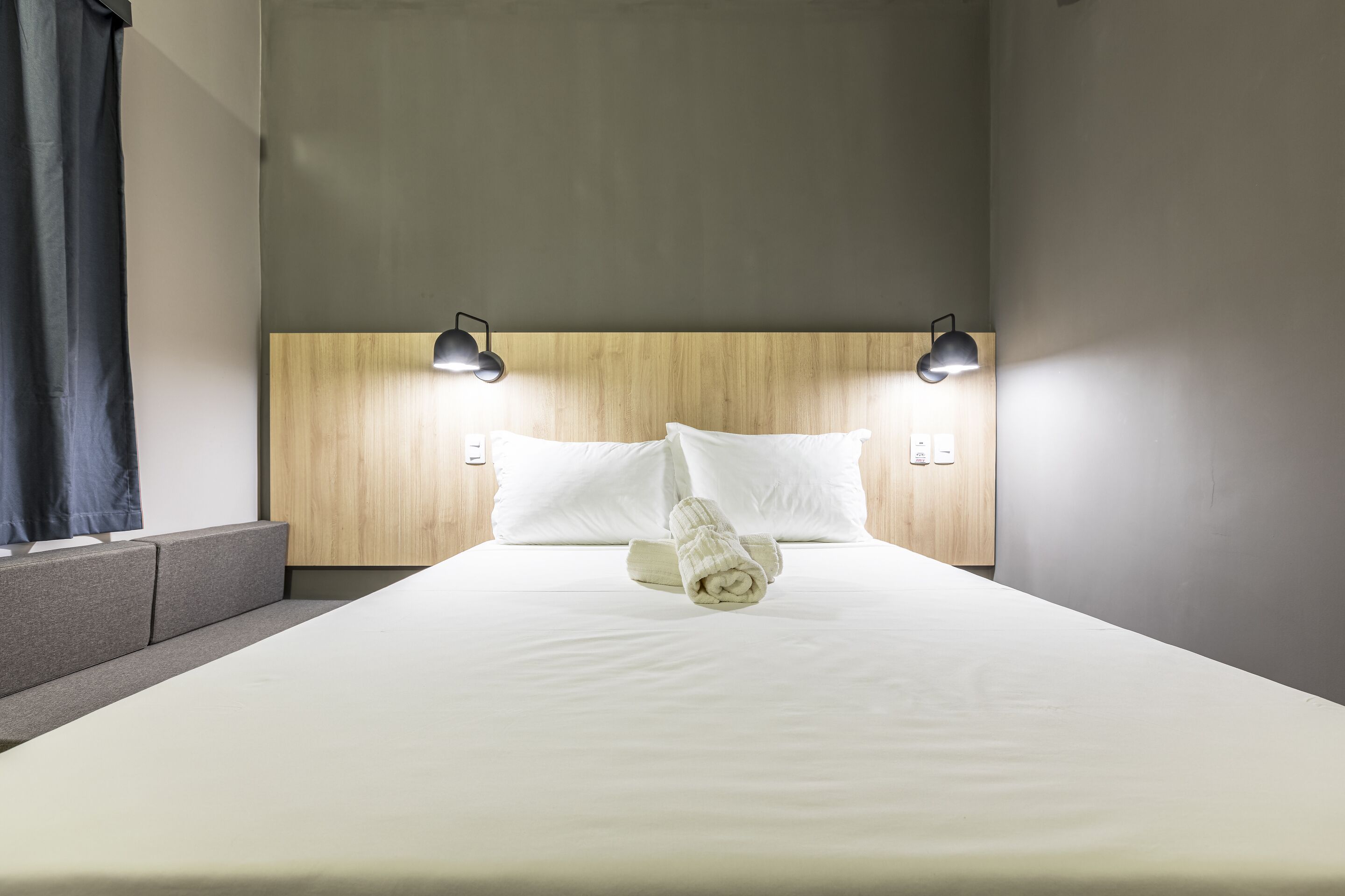 Una cama bien hecha con sábanas blancas, dos lámparas de noche y un cabecero de madera.