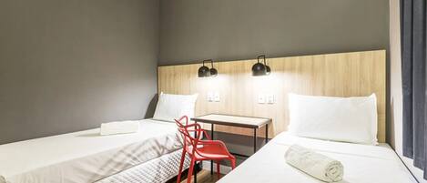 Habitación de hotel con dos camas, un escritorio, una silla roja y aire acondicionado instalado en la pared.