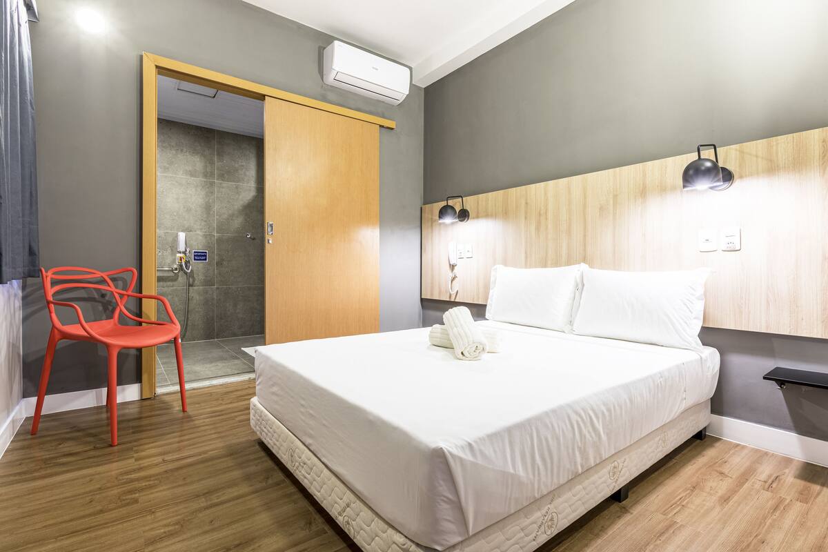 Ein Hotelzimmer mit Bett, einem roten Sessel, einem hölzernen Kopfteil und einer Duschkabine.