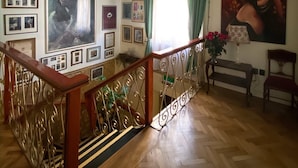 Una habitación amplia con una escalera de madera, una araña y una pared decorada con cuadros enmarcados y un cuadro grande.