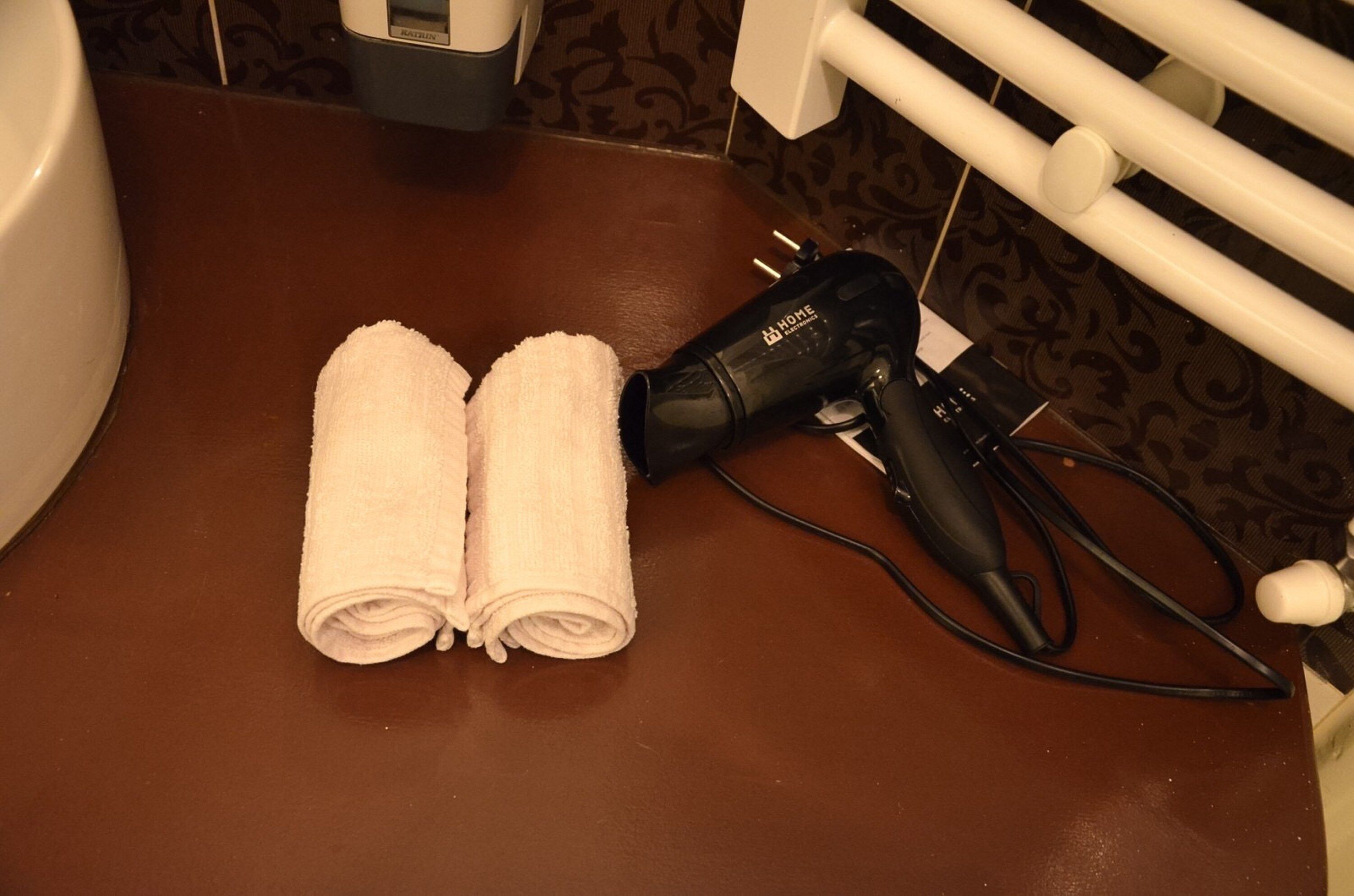 A bathroom with a brown countertop, two rolled towels, and a hair dryer.