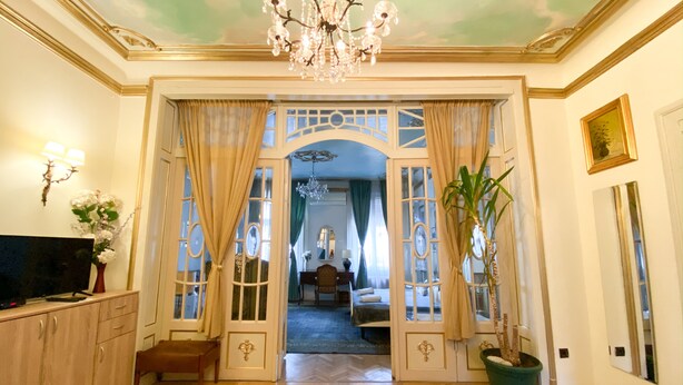 Un salón amplio con una araña, televisor y un comedor visible a través de un arco abierto.