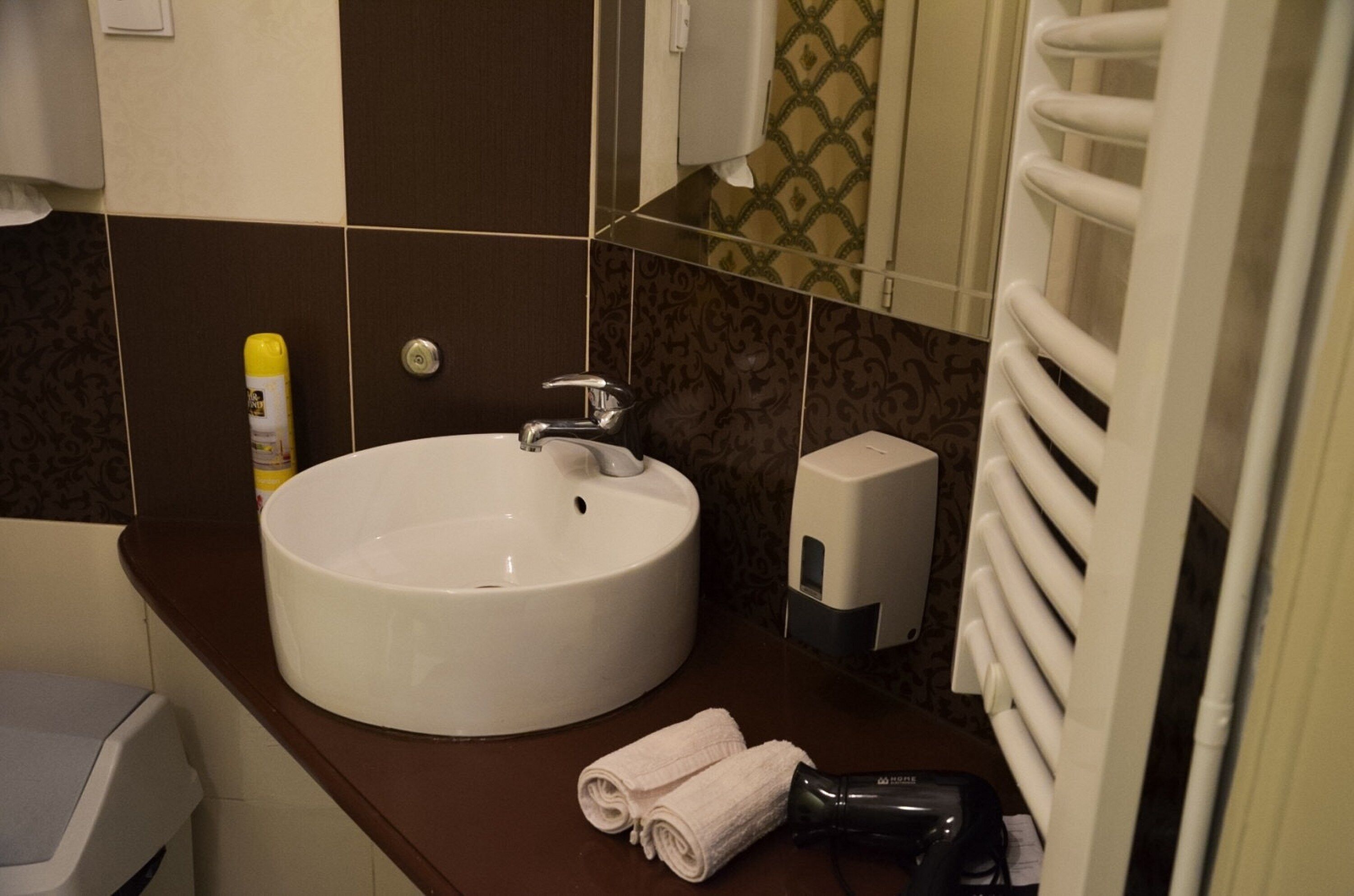 A bathroom with a white sink, a towel dispenser, and a hairdryer on the counter.
