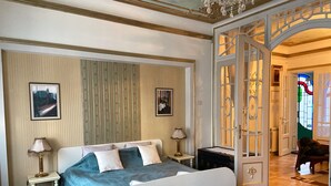 Un dormitorio con una cama grande, dos mesitas de noche con lámparas, una alfombra estampada y una puerta que da a otra habitación.