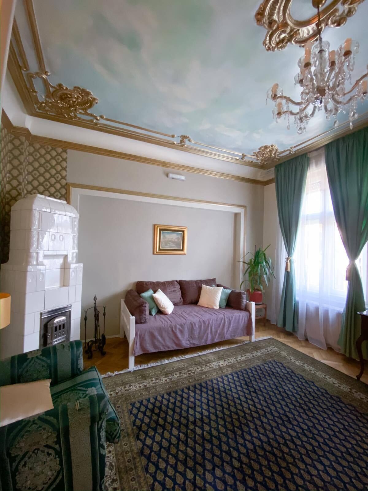 A room with a patterned carpet, a sofa with cushions, a chandelier, and a potted plant.