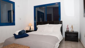 A neatly arranged bedroom with a bed, a nightstand, a lamp, and a window with blinds. - Villa Near the Beach (Paralimni)
