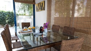 A glass-top dining table with wicker chairs, surrounded by a woven screen. - Villa Near the Beach (Paralimni)