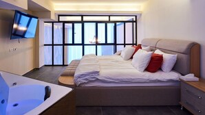 Habitació d'hotel moderna amb un llit gran, una televisió de pantalla plana, una banyera i una finestra ampla amb persianes.