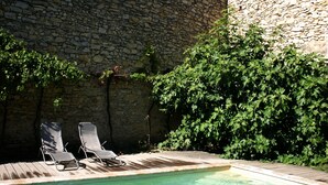 Una piscina con dos sillones de descanso, rodeada de muros de piedra y abundante vegetación.