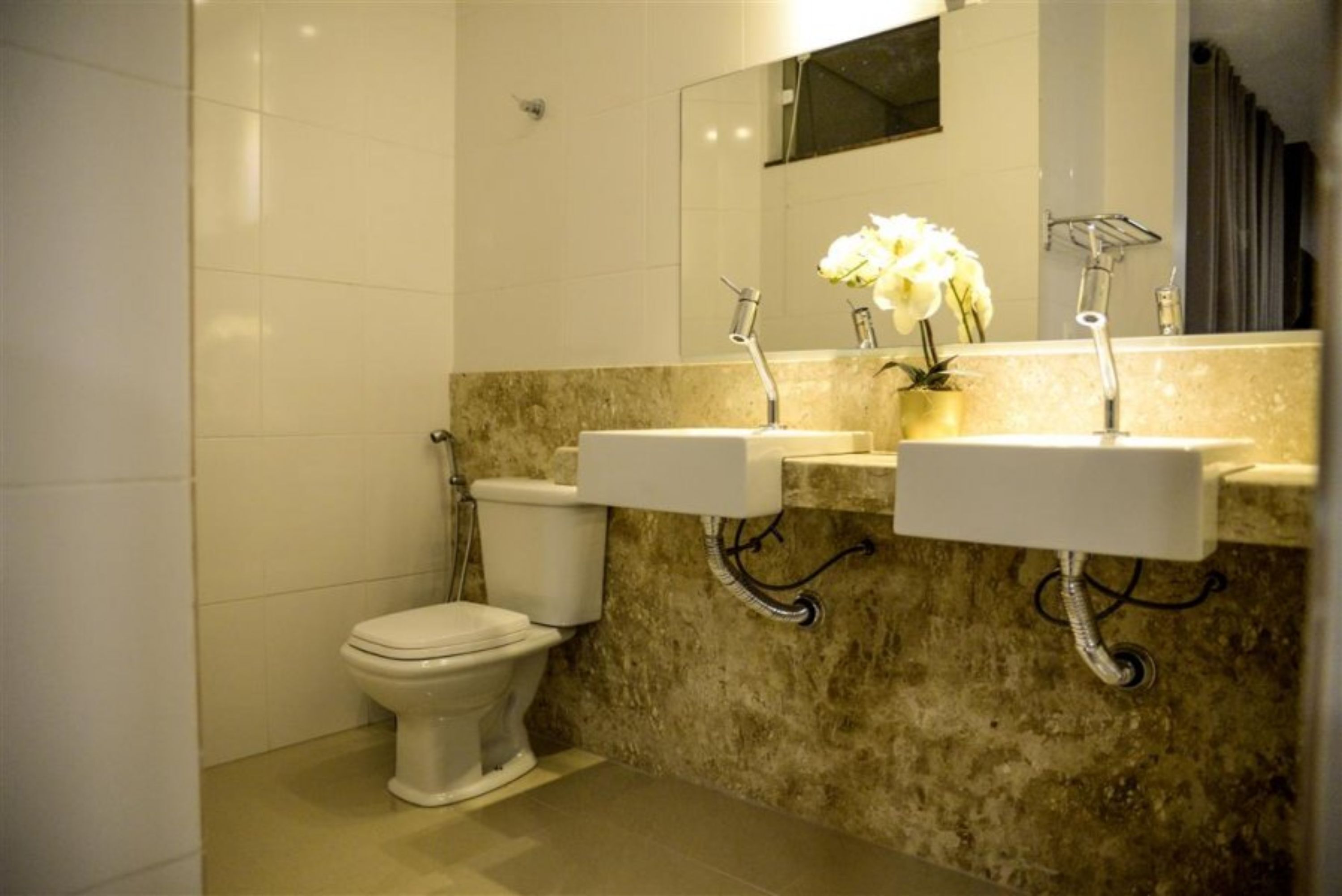Een badkamer met een toilet, twee wasbakken, een marmeren aanrechtblad en een spiegel.