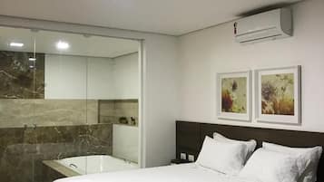 A modern bedroom with a large bed, a glass shower enclosure, and a mounted air conditioner.