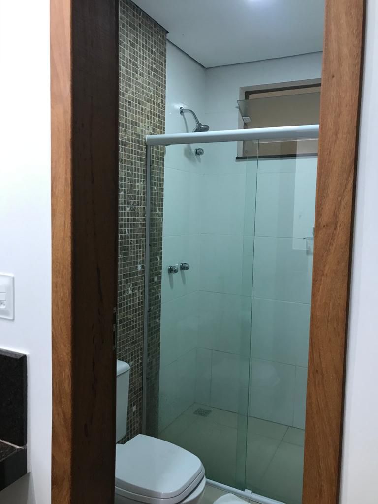 Une petite cabine de douche fermée, dotée d’une porte en verre, de toilettes blanches et d’un mur carrelé.