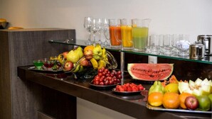 Un bufé con varias frutas, zumos y vasos sobre una repisa de vidrio.