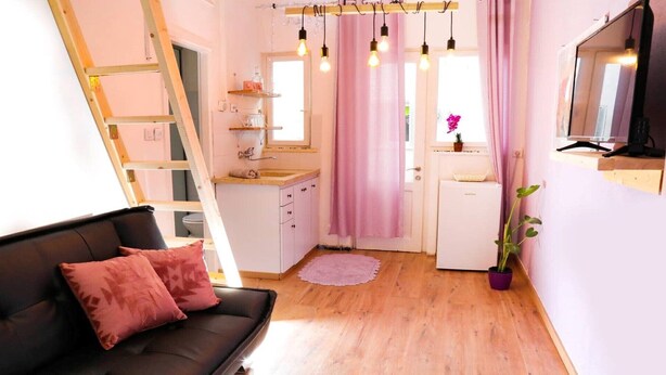 Ein gemütlicher, kompakter Wohnraum mit einer Couch, einer Küchenzeile, einem kleinen Kühlschrank und einem Fenster mit Vorhängen.