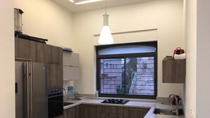 Eine moderne Küche mit Holzausstattung, einem eingebauten Backofen, einem Kühlschrank, einem Fenster mit Blick auf ein Gebäude und einer Pendelleuchte.