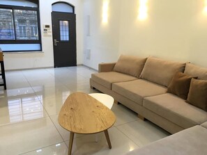 Un salon moderne avec un canapé beige, une table basse ronde en bois et une porte noire dotée d’une fenêtre.