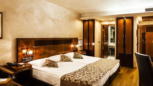 Une chambre d’hôtel avec un grand lit, des tables de chevet, un bureau et une chaise. La chambre est également équipée d’une armoire et d’un miroir.