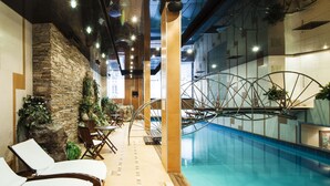 Une piscine intérieure dotée de chaises longues et d’un mur en pierre.