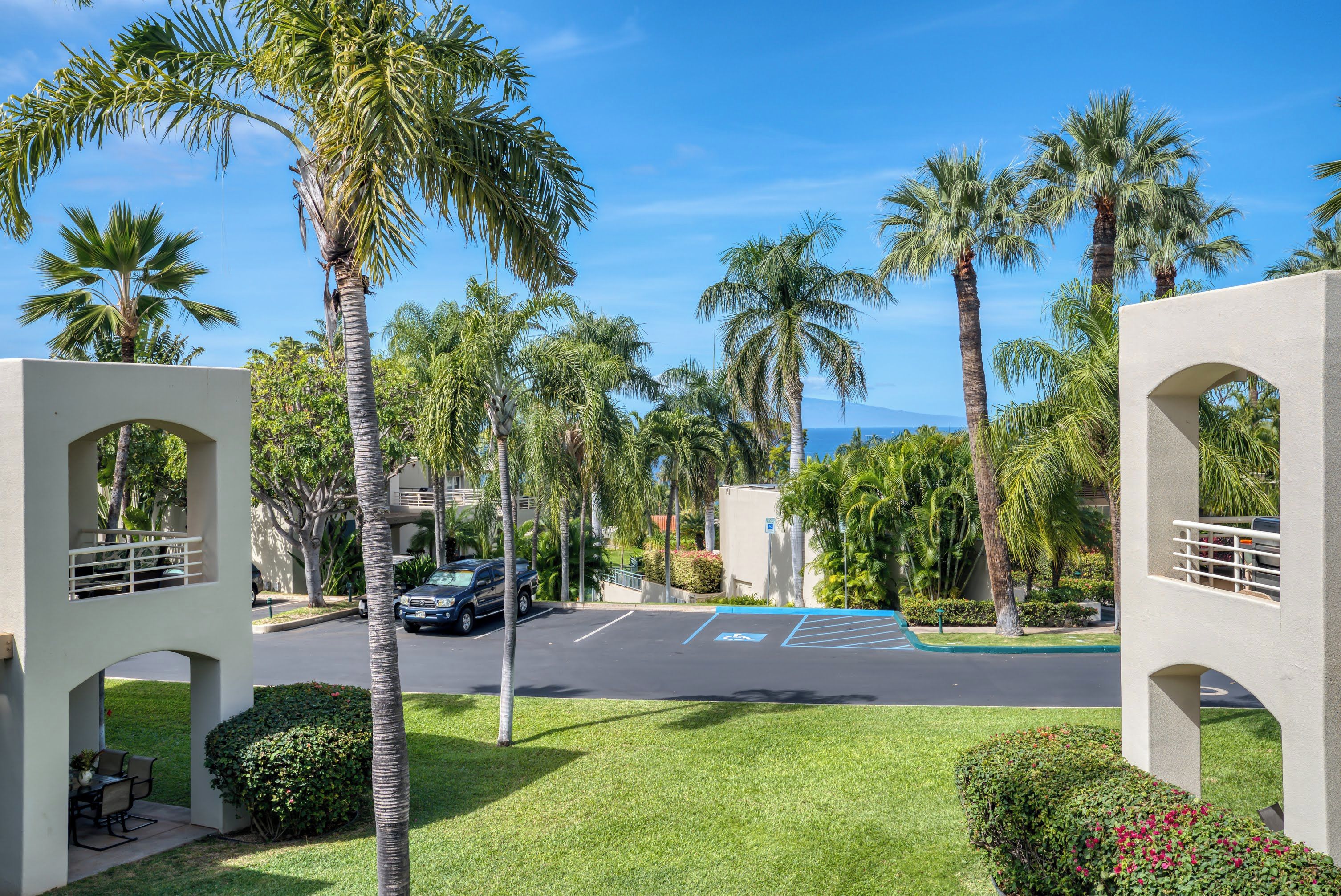 A parking area with palm trees, a car, and a building with arches.