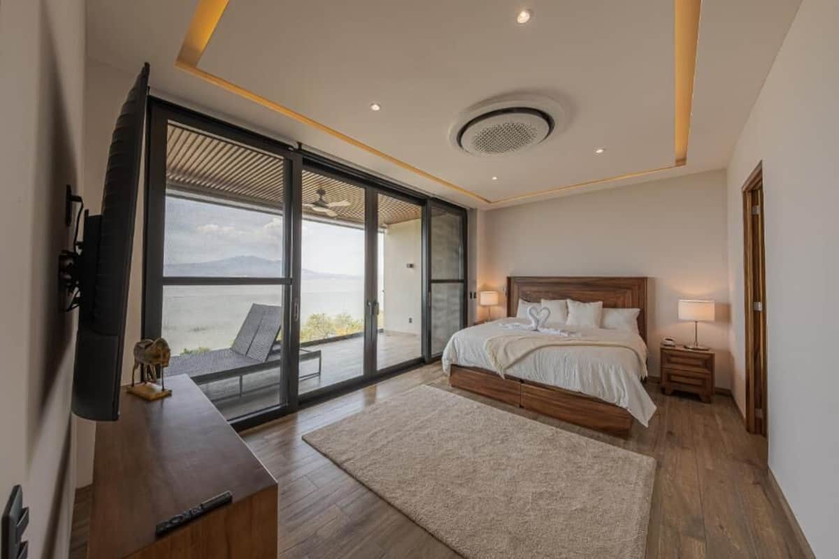 A bedroom with a bed, bedside tables, a TV, and a sliding glass door leading to a balcony.
