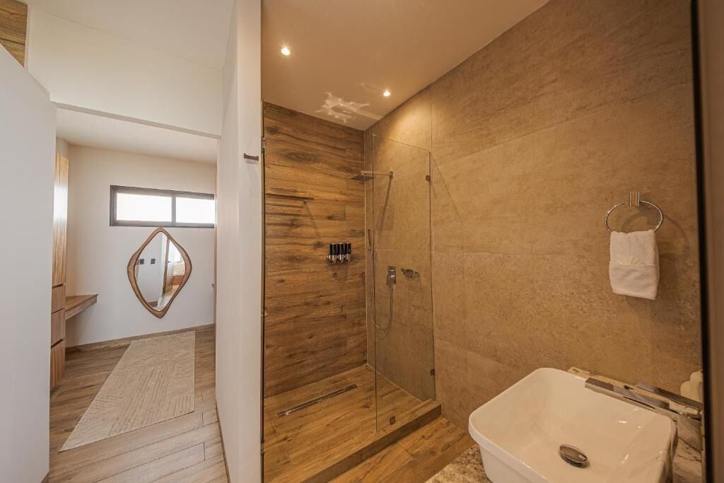Un baño moderno con ducha de vidrio, una bañera blanca y piso de madera.