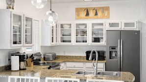 A modern kitchen with white cabinetry, a stainless steel refrigerator, a coffee maker, and a microwave. - Coral Reef - Private Beach, Bikes, & Beach Chairs (Santa Rosa Beach)