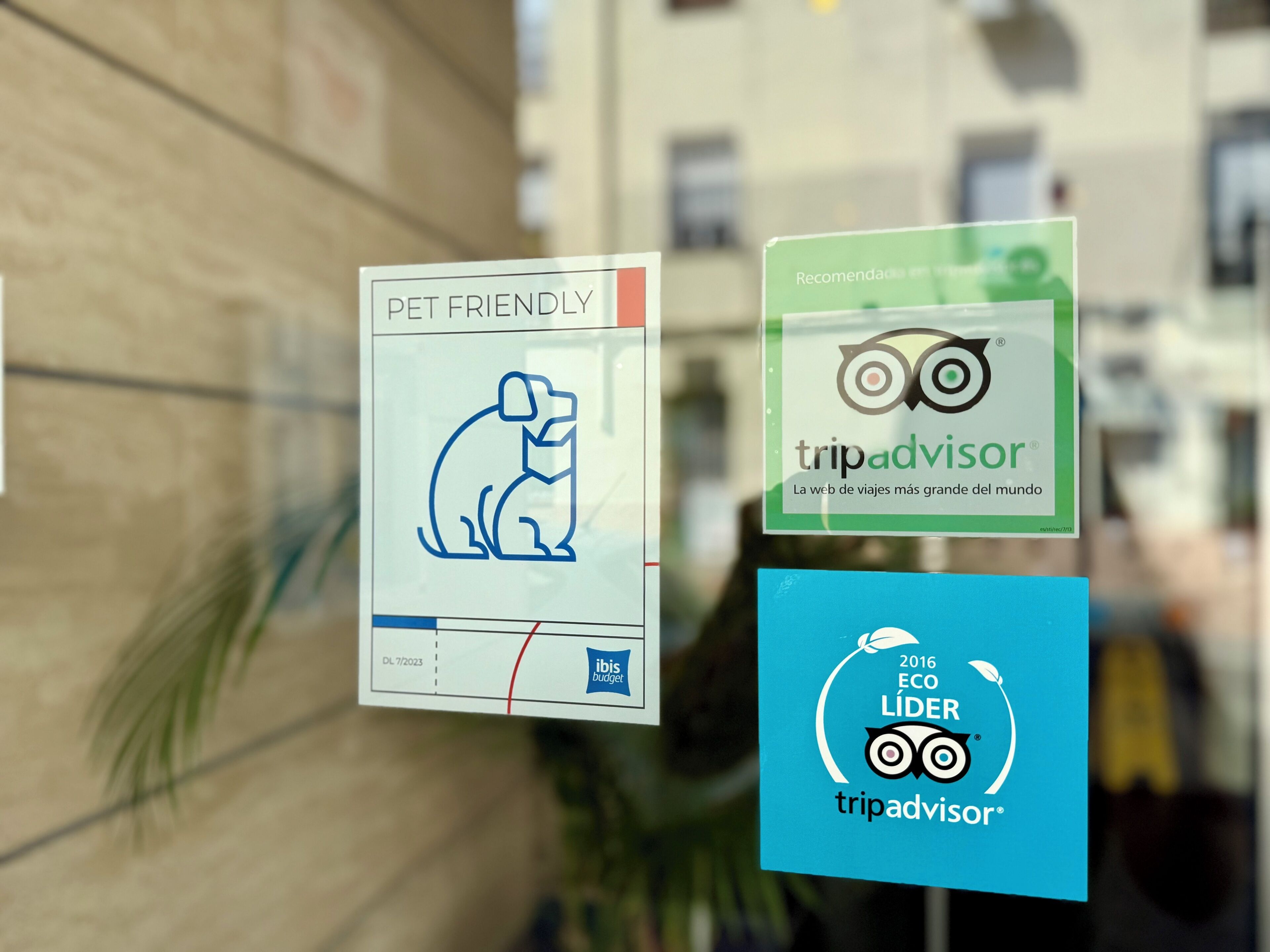 A glass window with multiple stickers, including a pet-friendly sign, a TripAdvisor logo, and an eco-leader logo.
