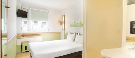 Habitación de hotel con cama, escritorio, televisión, baño con lavamanos y ventana.