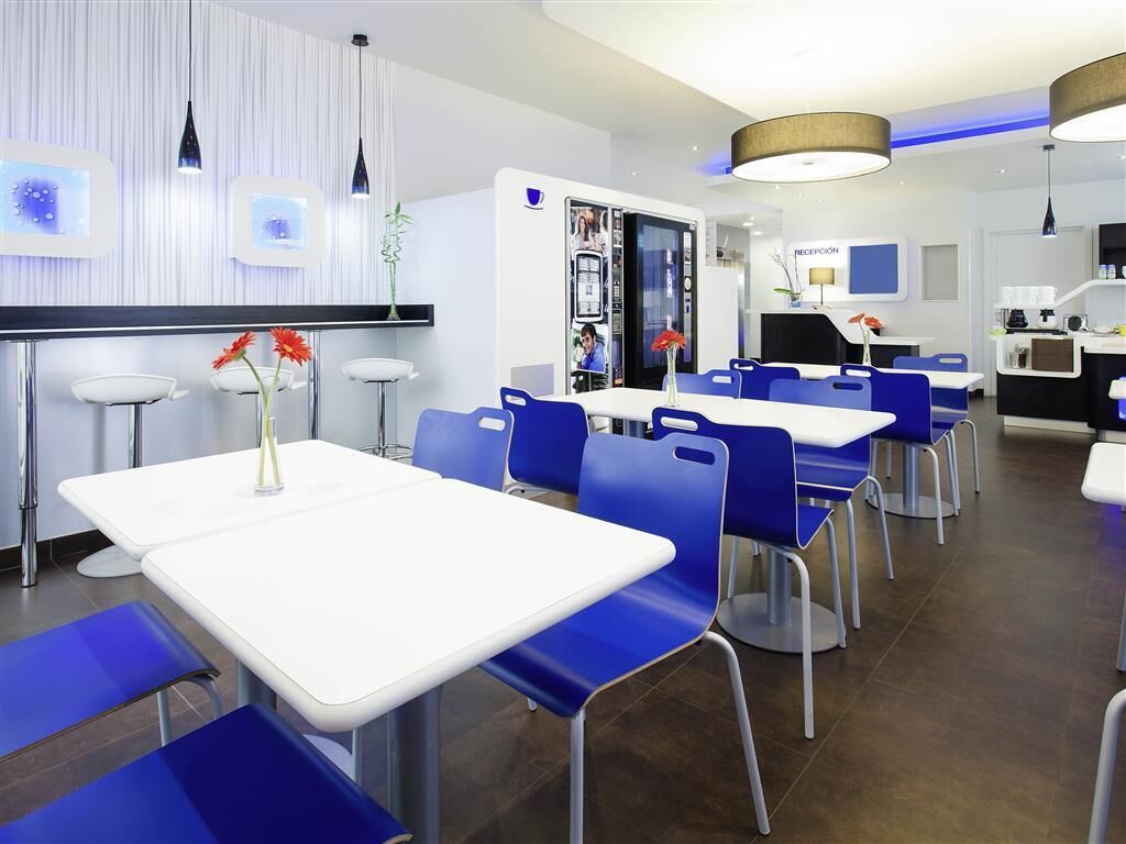 A modern dining area with white tables and blue chairs, a reception desk, and a counter with a coffee machine.