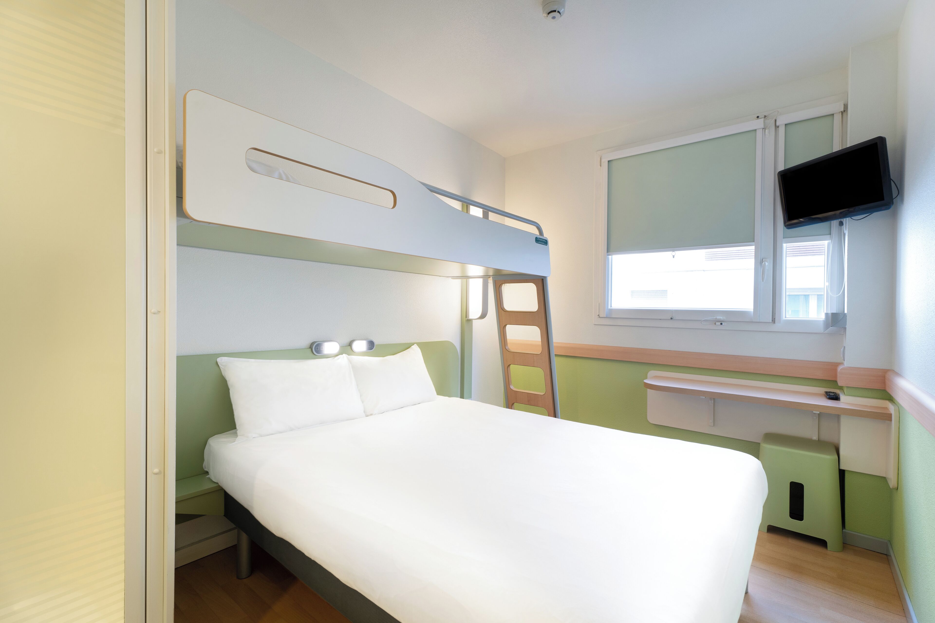 Ein Stockbett mit Schreibtisch und Fernseher in einem Zimmer mit grünen Wänden und einem Fenster.