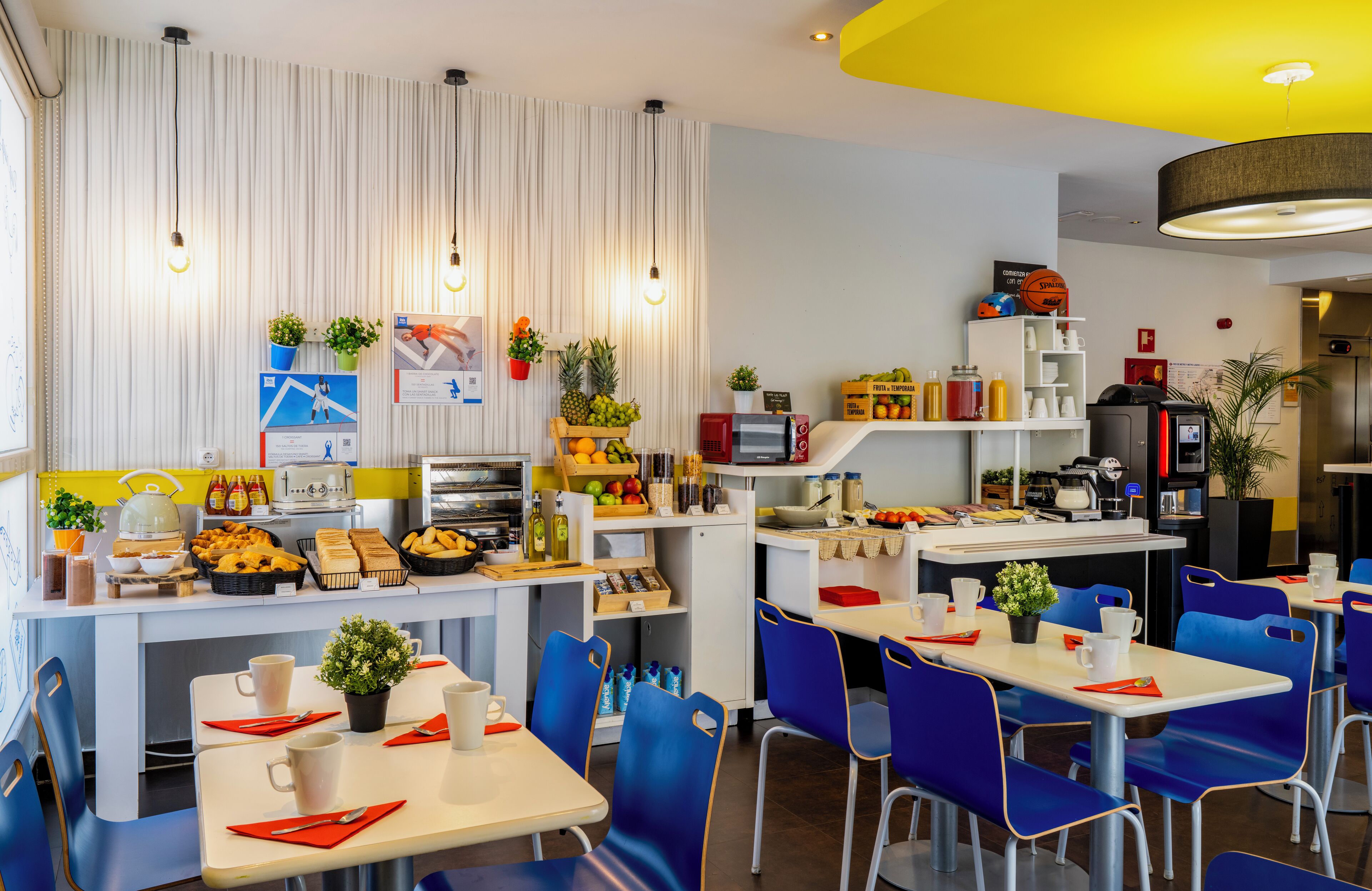 Un caffè moderno con arredamento blu e bianco, dotato di un bancone con diverse pietanze e un'area salotto con sedie blu e tavoli bianchi.