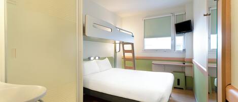Una habitación de hotel compacta con literas, un escritorio pequeño, un espejo y un televisor.