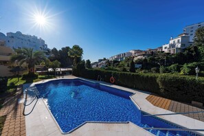 Ein Schwimmbecken mit klarem, blauem Wasser, umgeben von einer gepflasterten Terrasse und einem Heckenstreifen.