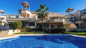 A swimming pool with a clear blue water surface, surrounded by a building with multiple balconies and a palm tree. - Jardines de Burriana 15 (Nerja)
