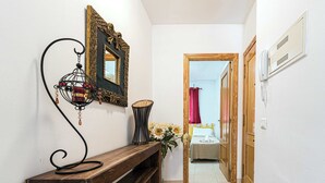 A hallway with a wooden bench, a mirror, a wall-mounted phone, and a door leading to a room with a bed and a window. - Jardines de Burriana 15 (Nerja)