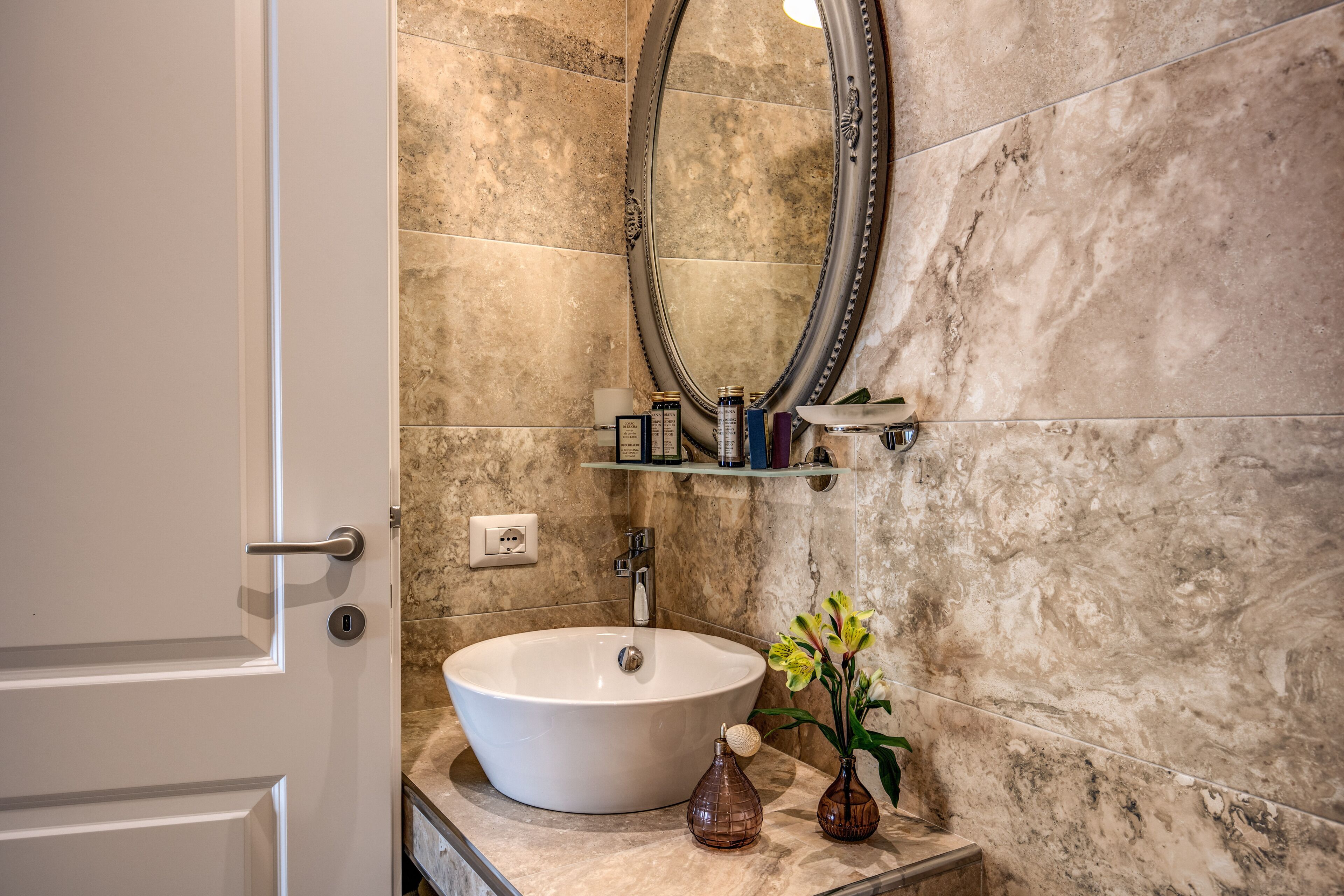 A bathroom with a white sink, a mirror, and a marble wall.