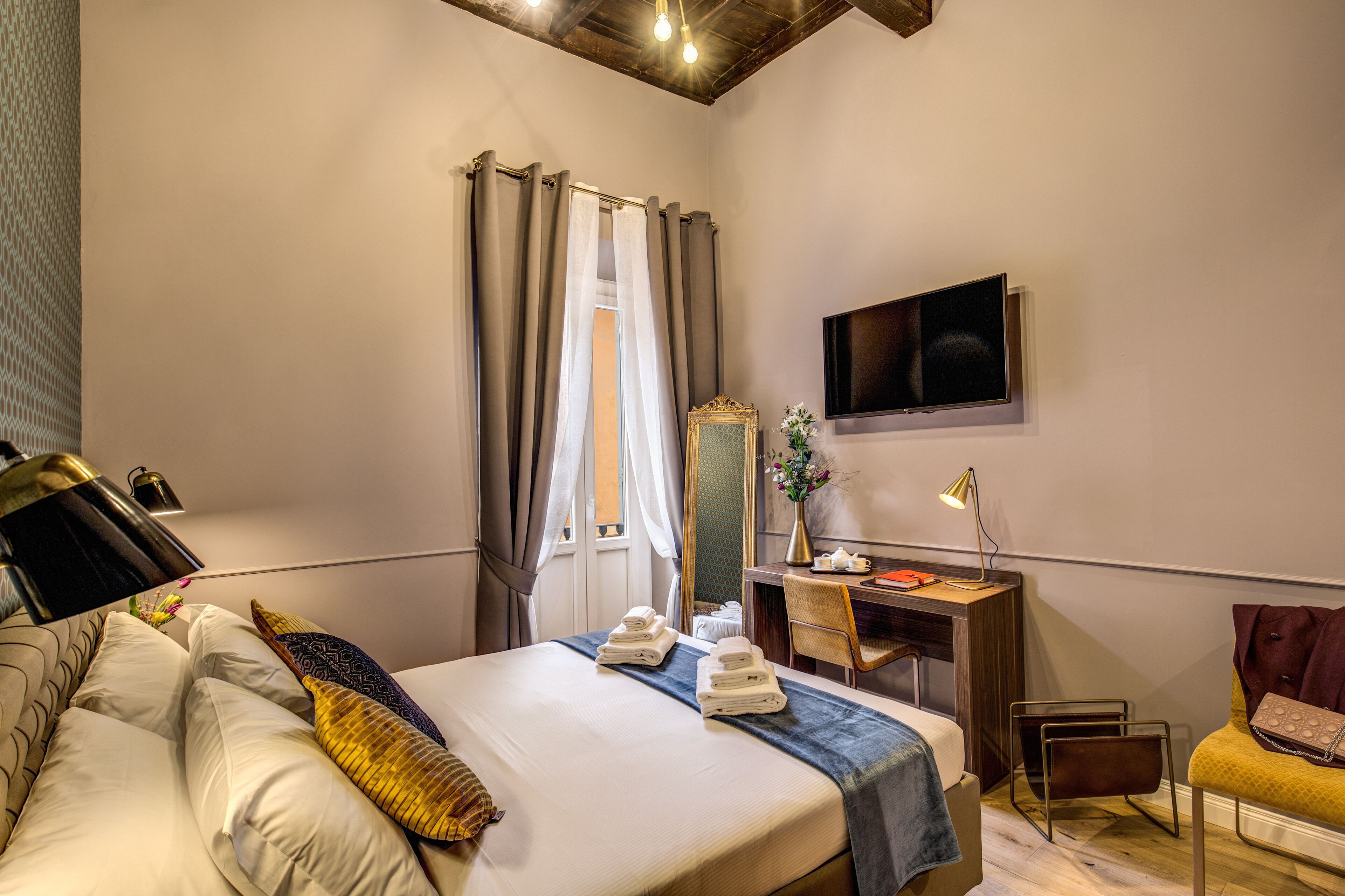 A hotel room with a bed, a desk, a chair, a TV, and a window with curtains.