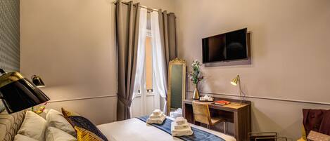A hotel room with a bed, a desk, a chair, a TV, and a window with curtains.