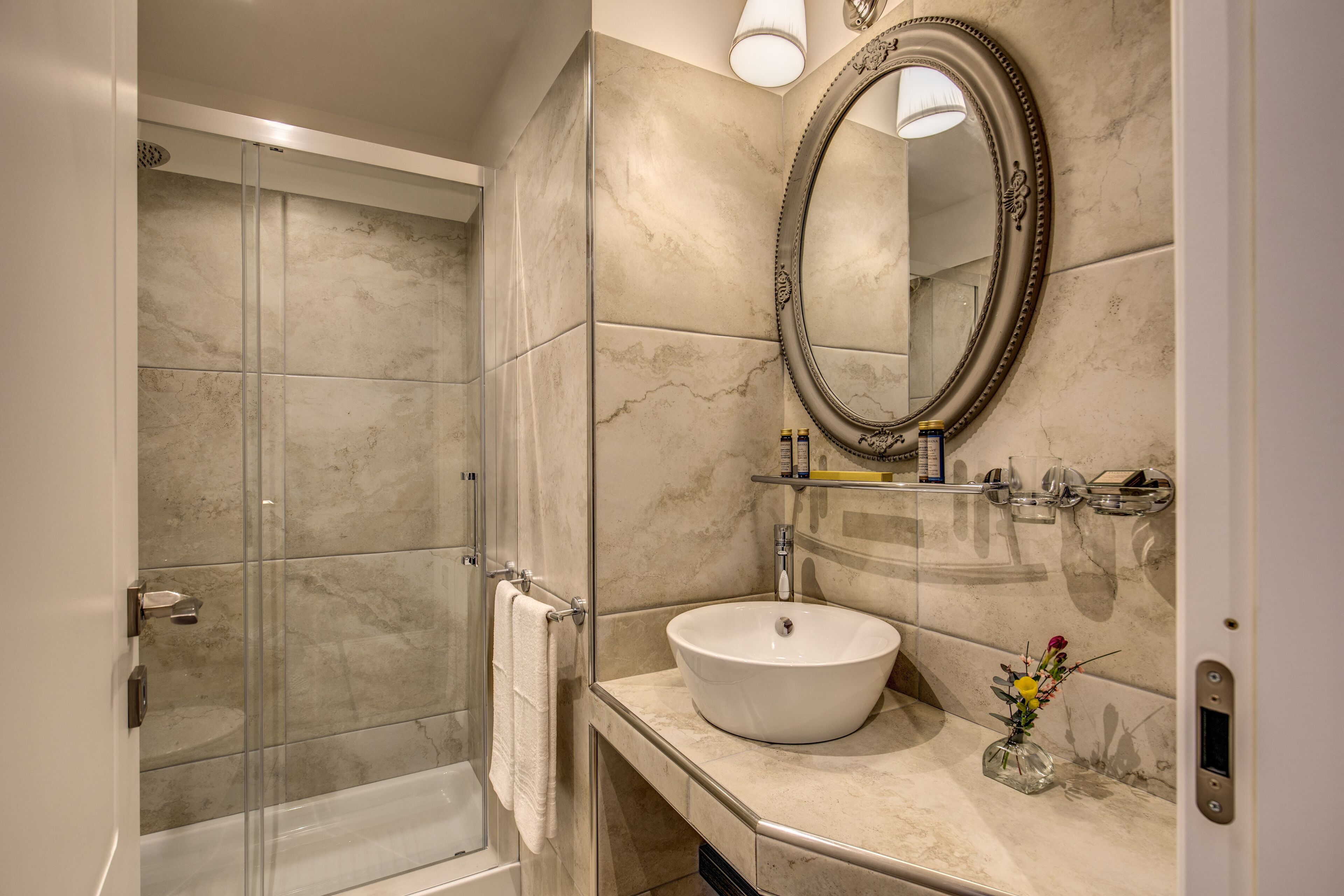 Un baño con ducha de vidrio, un lavamanos blanco y un espejo con marco decorativo.