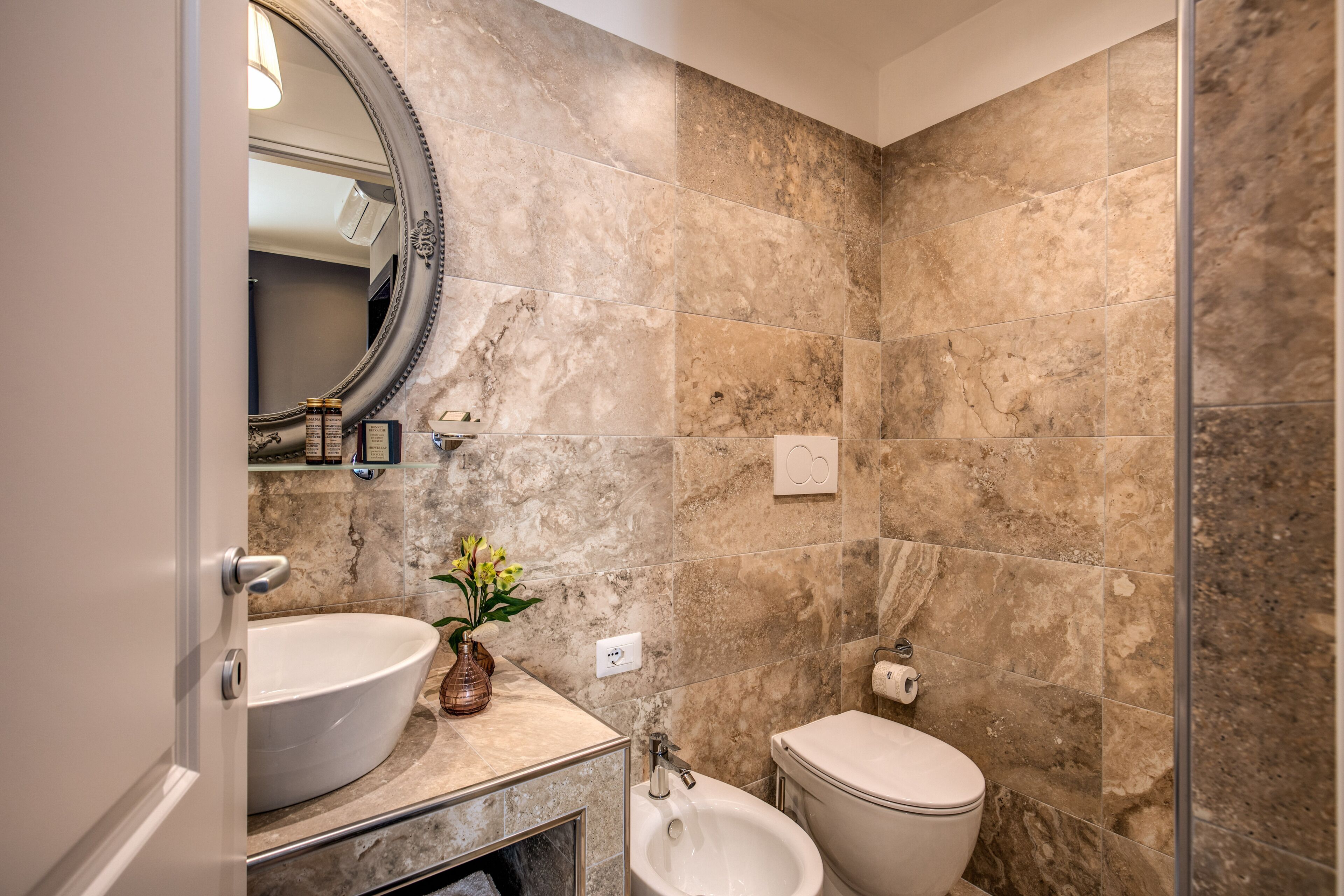 Un baño con un lavamanos ovalado grande, un bidé pedestal, un inodoro y un espejo con marco decorativo.