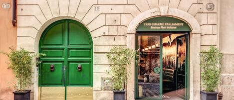 A building with two green doors, one of which has a sign reading "Tree Charme Parliament Boutique Hotel & Bistro".