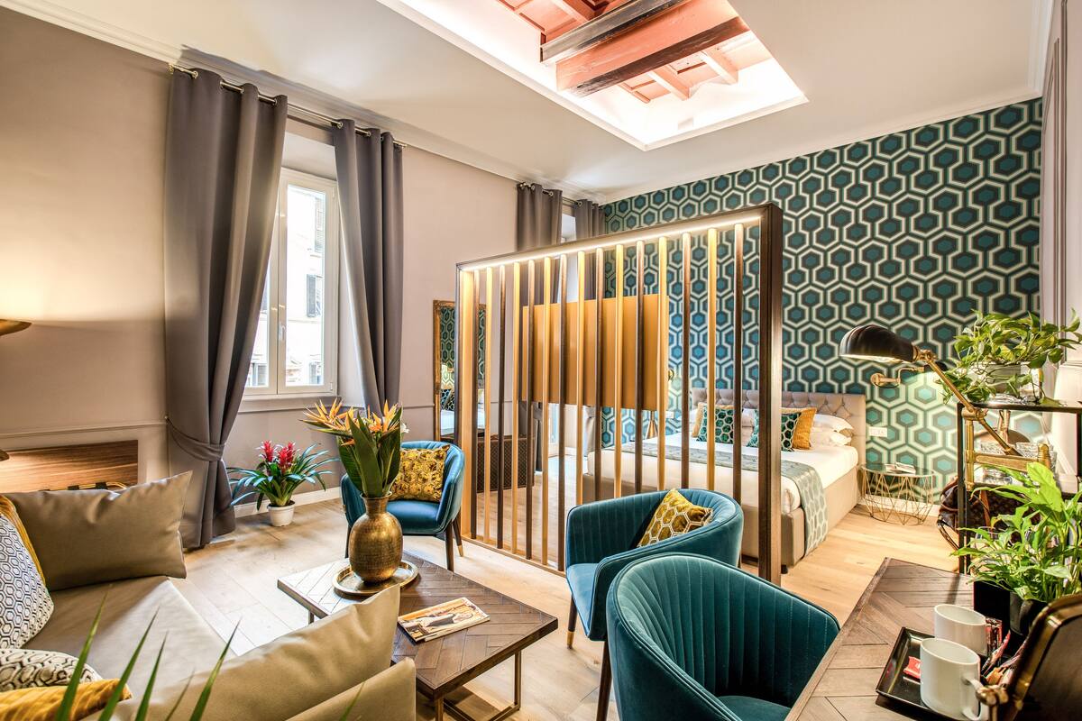 A modern hotel room with a sofa, armchairs, a coffee table, a bed, and a decorative partition.