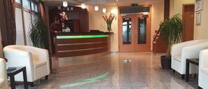 Uma área de recepção de hotel com um balcão curvo, dois sofás de couro branco e um vaso de planta.