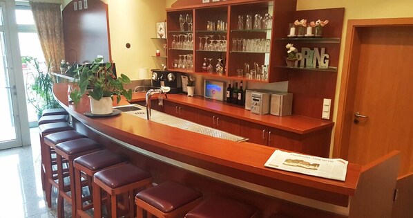 Zona de bar con mostrador de madera, taburetes y estanterías con cristalería.
