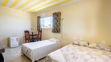 Un dormitorio con dos camas, una mesita, una silla, un refrigerador y una ventana con cortinas.