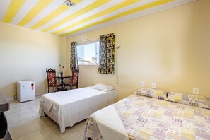 A bedroom with two beds, a small table, a chair, a refrigerator, and a window with curtains. - OYO Pousada Cavalo Marinho (Baia da Traicao)