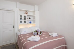 A neatly arranged bedroom with a bed, pillows, a bedside table with a vase, and a door. - Santorini Folia Bianca (Santorini)