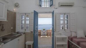Eine kompakte Küche mit Blick auf einen Balkon, ein Essbereich mit Tisch und Stühlen sowie ein Bett mit Wandverkleidung aus Stein.