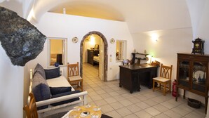 Ein gemütliches Wohnzimmer mit Sofa, Sesseln, Couchtisch und Kamin. Ein Flur führt in einen weiteren Raum.